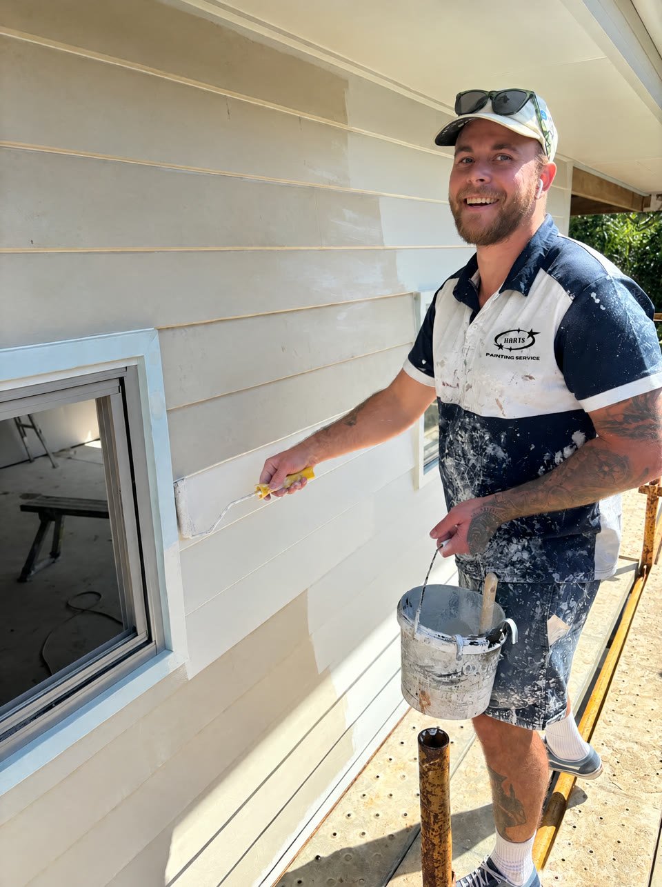 Harts painter rolling fresh paint onto exterior weatherboards from the scaffold